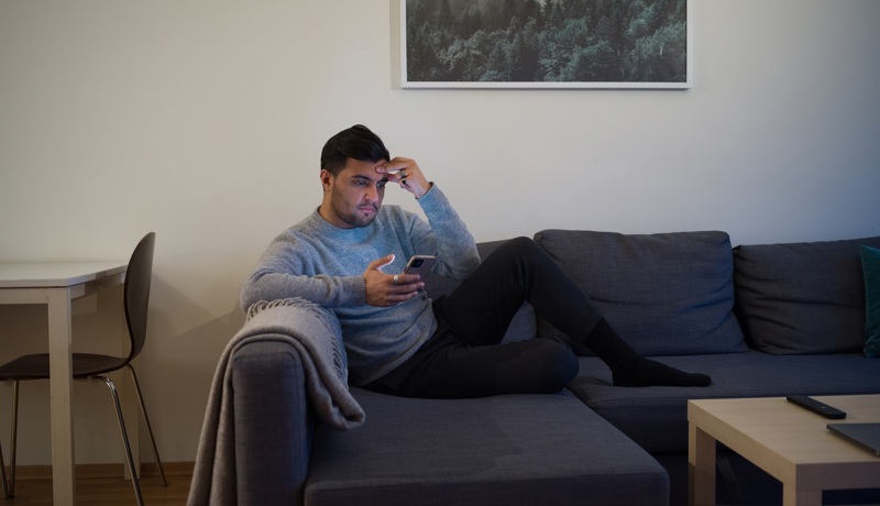En man som sitter i soffan och scrollar på sin mobil